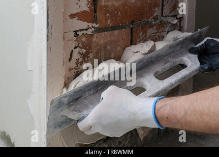 Worker's hands are using long trowel for gypsum plaster. Stock Photo