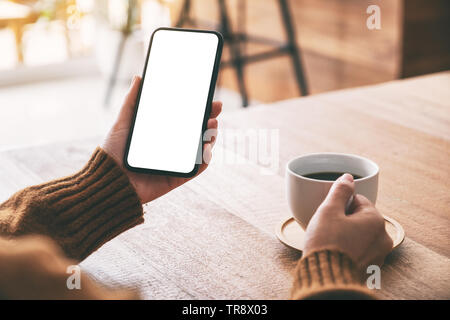 Mockup image of woman's hand holding black mobile phone with blank screen while drinking coffee Stock Photo