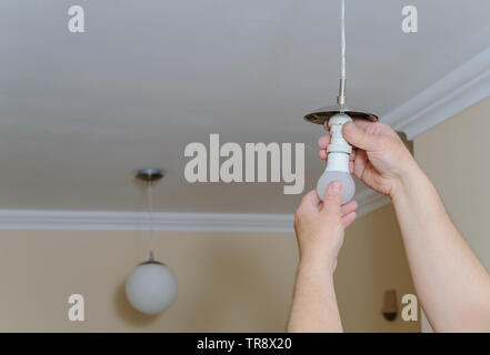 Electrician's hands are installing a LED light bulb in a lamp. Stock Photo