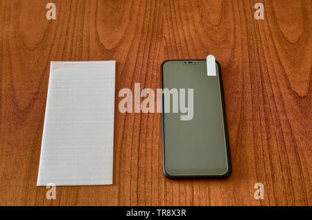 On the wooden table, the smartphone and the protective glass cover for the screen. The protective glass was placed on the display for testing. The fil Stock Photo