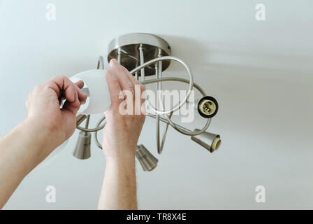 Electrician's hands are installing a LED light bulb in a lamp. Stock Photo