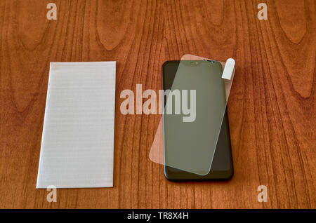 On the wooden table, the smartphone and the protective glass cover for the screen. The protective glass was placed on the display for testing. The fil Stock Photo