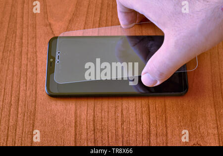 The hand of a Caucasian man gently rests the protective glass on the display of the smartphone. Stock Photo