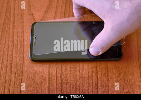 The hand of a Caucasian man gently rests the protective glass on the display of the smartphone. Stock Photo