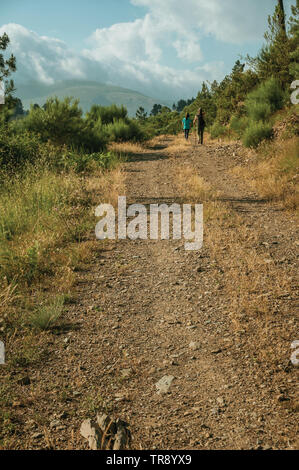 People hiking on dirt road over hilly terrain with trees, at the highlands of Serra da Estrela. The highest mountain range in continental Portugal. Stock Photo