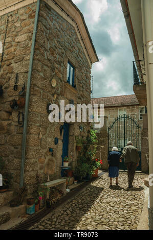 Elderly couple walking by alley with old houses at Alvoco da Serra. A cute village clinging on a steep valley in eastern Portugal. Stock Photo