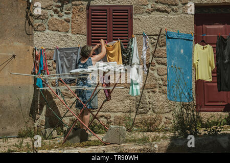 Old woman hanging clothes to dry in front of old house at Belmonte. Birthplace of the discoverer Pedro Cabral in Portugal. Stock Photo
