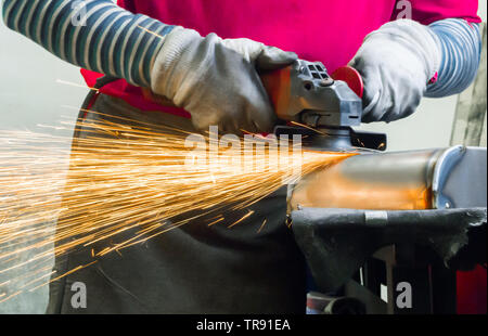 Metalworker in a pink t-shirt grinding metal using angle grinder, hot sparks flying around. Stock Photo