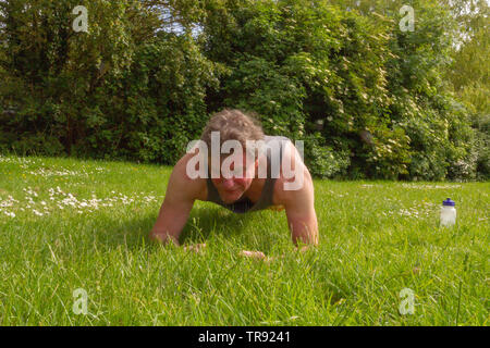 Baby boomer performing the "plank" exercise outdoors in a park. Healthy outdoors lifestyle concept. Stock Photo