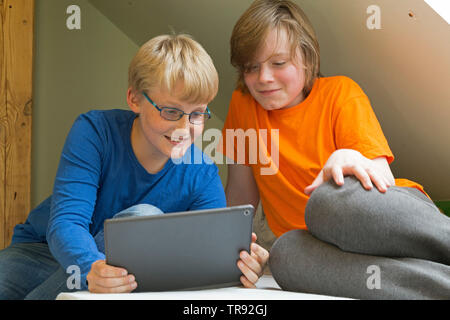 boy plyaing with tablet computer, his friend watching, Germany