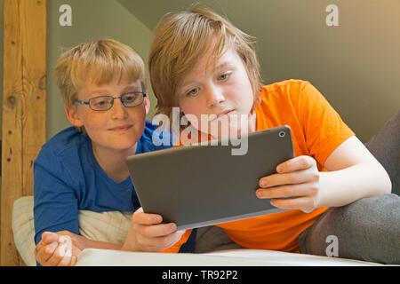 boy plyaing with tablet computer, his friend watching, Germany