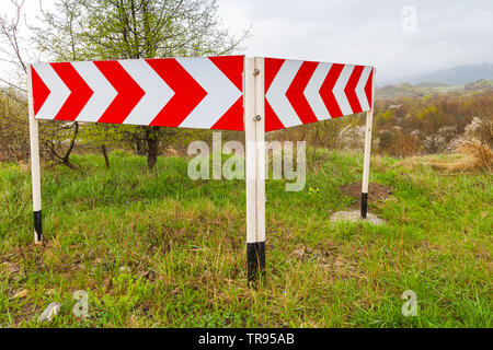 Dangerous turns. Red and white striped arrows. Road sign mounted on a roadside of a mountain road Stock Photo