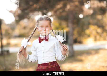 Smiling pupil girl 6-7 year old posing outdoors wearing school uniform. First grade. Back to school. Stock Photo