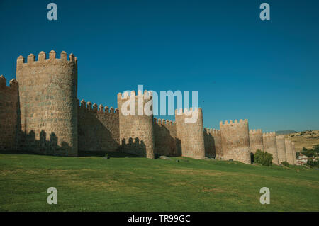 Lined stone towers on the large city wall in Romanesque style and green lawn at Avila. With an imposing wall around the gothic city center in Spain. Stock Photo