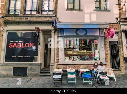 Two people sitting down at a table outside The Coco doughnut shop, a small café in the Sablon district of Brussels,Belgium Stock Photo