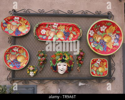 Colourful, hand-painted ceramics, one of the local crafts for sale to tourists in the hilltop town of Orvieto in Umbria; display of red plates on wall Stock Photo