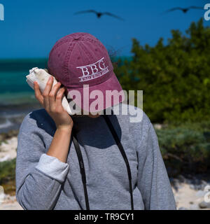 Woman holding conch shell close to her ear, Half Moon Caye, Lighthouse Reef Atoll, Belize Stock Photo