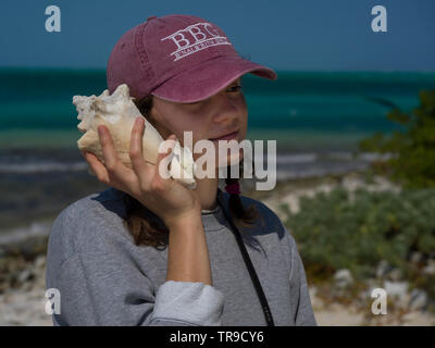 Woman holding conch shell close to her ear, Half Moon Caye, Lighthouse Reef Atoll, Belize Stock Photo