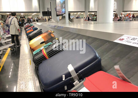 Luggage conveyor belt with personal suitcases moving around circle. Multiracial people waiting for their luggage. Hong Kong International Airport. Stock Photo