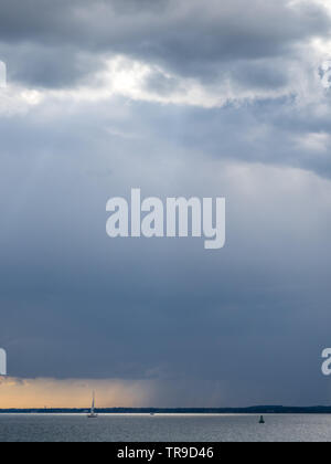 a rainfront moving approaching over Solent with lone single yacht sailing in sea with buoy under big sky storm clouds orange sunset Stock Photo