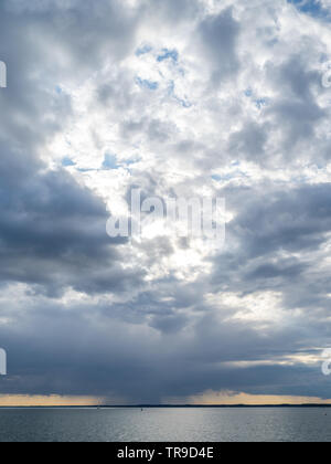 a rainfront moving approaching over Solent with lone single yacht sailing in sea with buoy under big sky storm clouds orange sunset Stock Photo