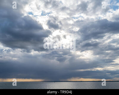 a rainfront moving approaching over Solent with lone single yacht sailing in sea with buoy under big sky storm clouds orange sunset Stock Photo
