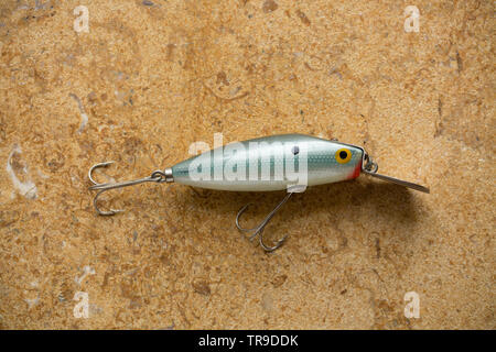 A vintage fishing lure equipped with treble hooks photographed on a stone background. These type of lures are often called plugs and are designed to c Stock Photo