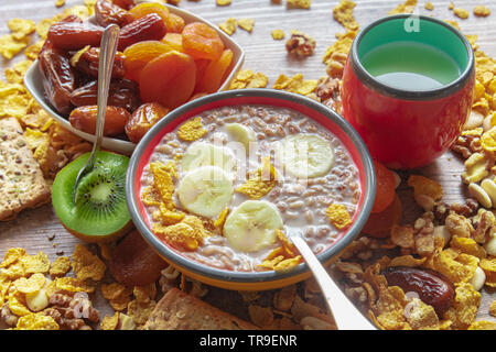 traditional breakfast served in bowls - dried and date plums, banana, cereal, kiwi, milk on a wooden table Stock Photo