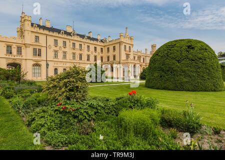 Lednice, Czech Republic - May 27 2019: Famous Lednice castle in South Moravia with yellow facade. Garden with green lawn, bush and flowers. Stock Photo