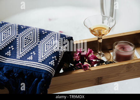 wooden shelf on the bathtub with glass of white wine, pink flowers and natural bath accessories Stock Photo