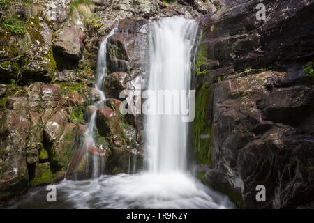 Close up view of a scenic waterfall on Old mountain in Serbia cascading down the red, wet rocky cliff covered by sunlit moss Stock Photo