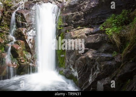 Close up view of a scenic waterfall on Old mountain in Serbia cascading down the red, wet rocky cliff covered by sunlit moss Stock Photo