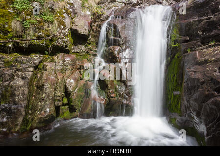 Close up view of a scenic waterfall on Old mountain in Serbia cascading down the red, wet rocky cliff covered by sunlit moss Stock Photo