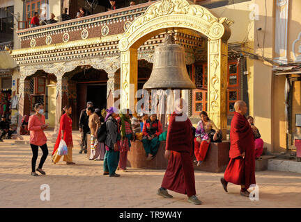 Buddhist monks pass by big bell in front of Tibetan Buddhist monastery at Boudhanath, Kathmandu Valley, Nepal Stock Photo