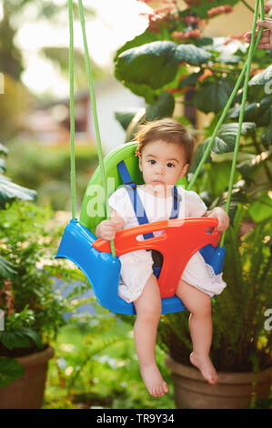 Little baby girl portrait sit on swings in bright sunny day Stock Photo