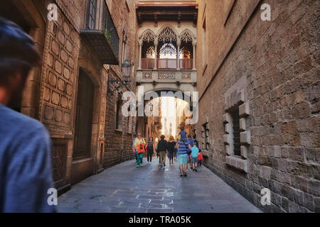 People walking on a narrow street near the ancient Bishop's Bridge in Carrer del Bisbe. Barcelona, Spain. Stock Photo
