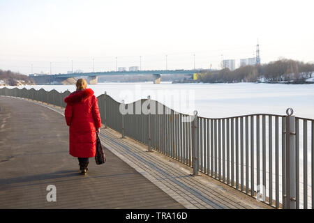 A lonely woman in a red coat walks along the promenade. Back view. Stock Photo