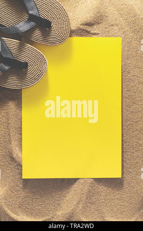Top view of flip flops and yellow color mockup for design on the sand. Copy space, vertical image. Summertime concept. Stock Photo