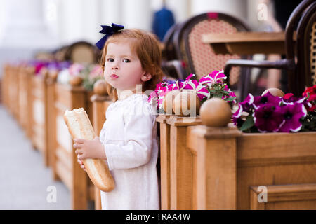 Funny baby girl 1-2 year old eating bread outdoors. Looking at camera. Stock Photo