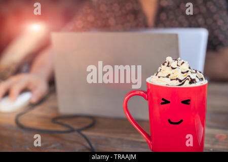 hot mocha coffee in red cup with smile face on wooden table with working man using laptop Stock Photo