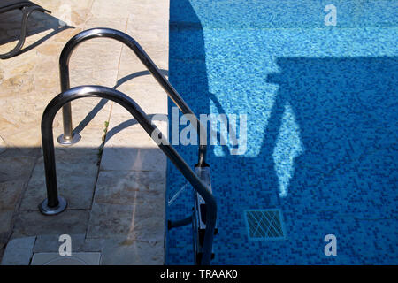 Handrail on pool. Swimming pool with stair at tropical resort. Pool handrails view. Water swimming pool with sunny reflection. Steel handrail. Stock Photo