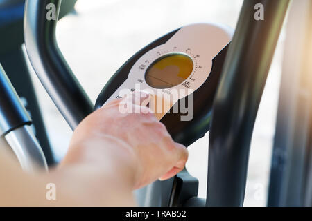 finger pressing on button of elliptical bike machine in fitness gym Stock Photo