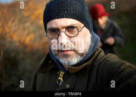 Middle aged handsome man wearing a Barbour wax jacket taking a selfie whilst out on a long walk in the hills and forest Stock Photo