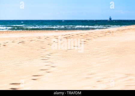 Footprints at white wide dune sand toward shore of sea,  view to small silhouette of far away ship at background horizon (copy space) Stock Photo