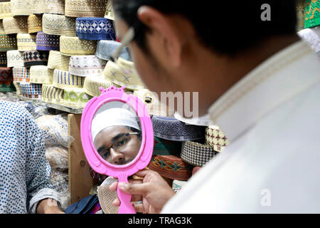 Dhaka, Bangladesh - June 01, 2019: A customer trying a tupi or prayer cap at a shop at the Baitul Mukarram National Mosque market ahead of the Eid-ul- Stock Photo