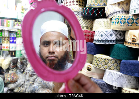 Dhaka, Bangladesh - June 01, 2019: A customer trying a tupi or prayer cap at a shop at the Baitul Mukarram National Mosque market ahead of the Eid-ul- Stock Photo