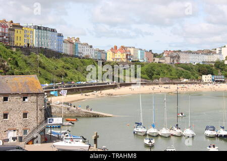 A photograph of Tenby harbour, Pembrokeshire, Wales, UK.  Boats, people enjoying the sunny weather, cliffs and buildings in the background.