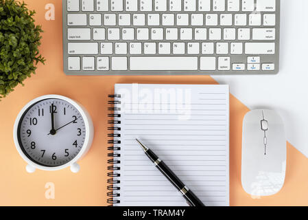 Directly above shot of office desk with potted plant, computer keyboard and mouse, note pad, alarm clock and pen on multicolored background. Stock Photo