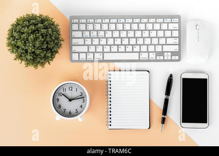 Directly above shot of office desk with potted plant, computer keyboard and mouse, smart phone, alarm clock, note pad and pen on multicolored backgrou Stock Photo