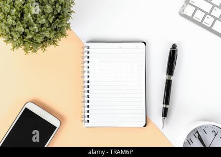Directly above shot of office desk with potted plant, computer keyboard smart phone, alarm clock, note pad and pen on multicolored background. Stock Photo